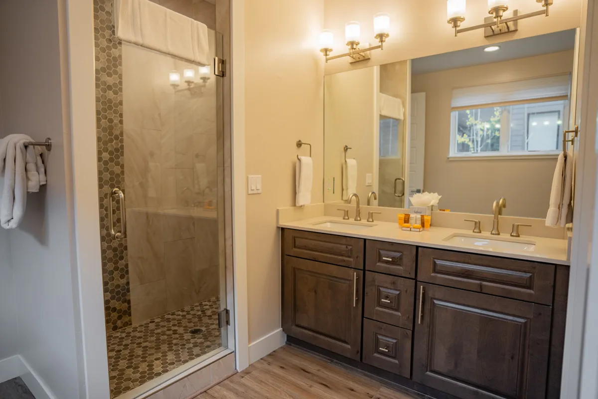 A modern and inviting bathroom with a double sink vanity, framed mirror, and a glass shower enclosure. The arrangement is bright and practical, designed to accommodate multiple guests easily.