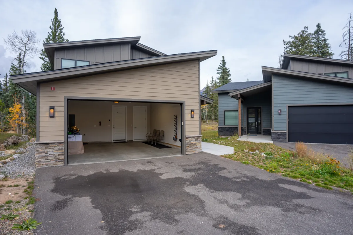 A modern standalone home framed by lush greenery, featuring a welcoming garage and ample space in front. The surrounding landscape hints at privacy and direct access to nature, ideal for group gatherings and outdoor relaxation.