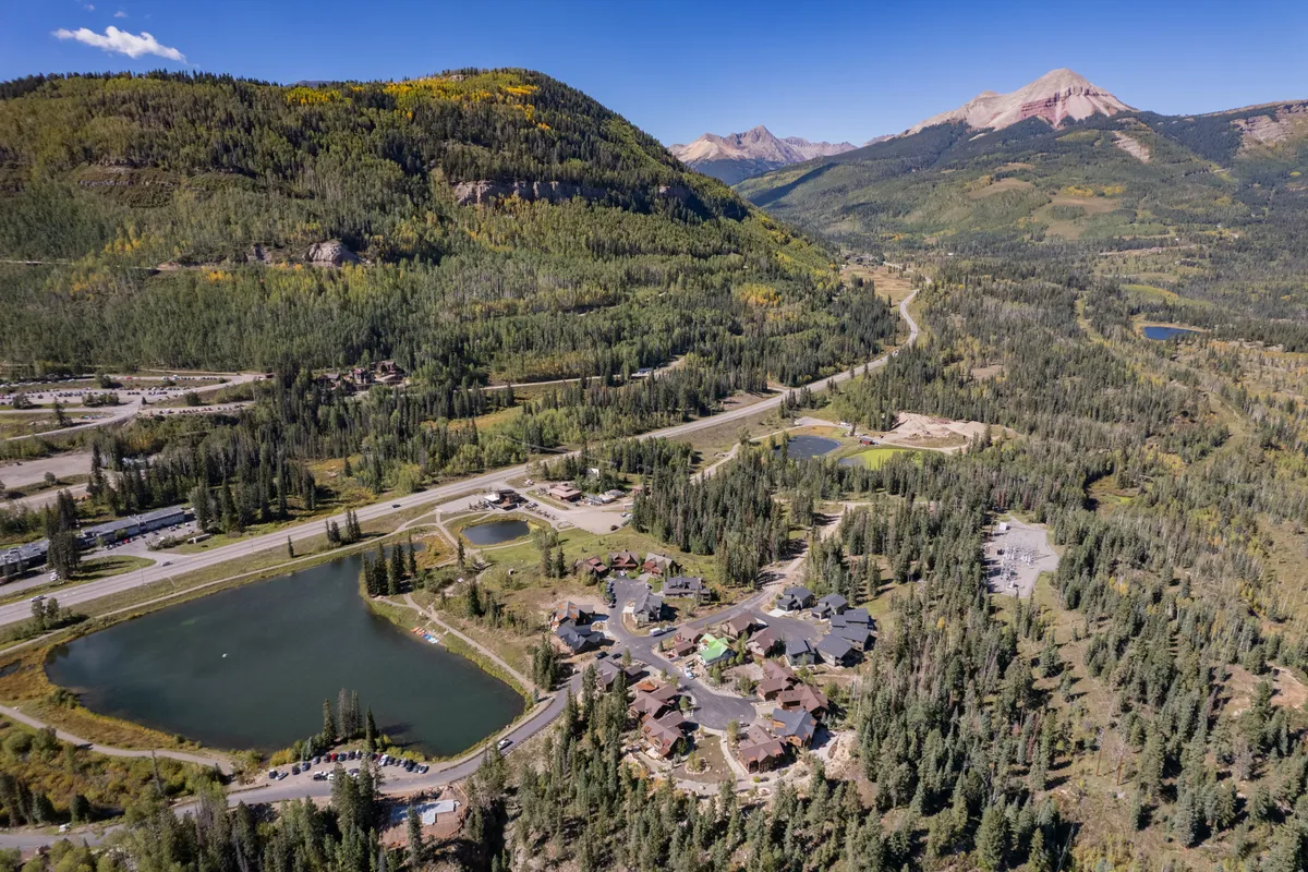 A wide-angle view showcasing the scenic mountain landscape, tranquil lakes, and residential areas surrounded by forested greenery. The image exudes a sense of connection to nature and adventure, with visible roadways suggesting ease of access to outdoor activities.