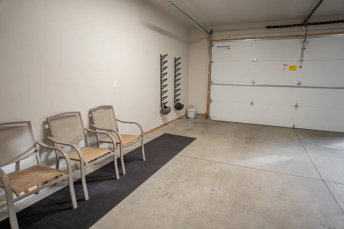 This image showcases an interior view of the garage, featuring a visible garage door, a storage rack, and chairs. The space appears organized and functional, offering ample room for vehicles as well as gear or equipment.