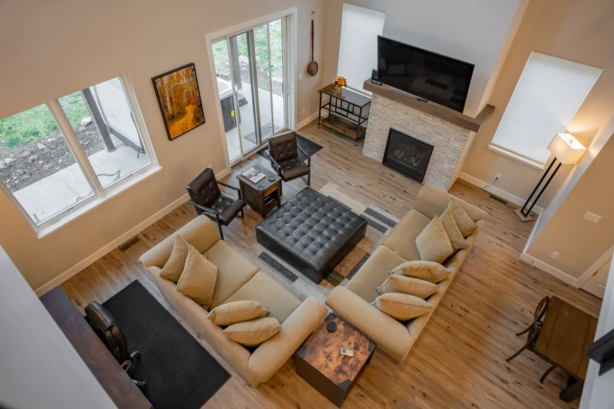 A spacious living room featuring a large sectional sofa, cozy fireplace, coffee table, and big windows offering views of the outdoors. The atmosphere is warm and comfortable, inviting guests to relax, watch movies, or engage in game nights together.