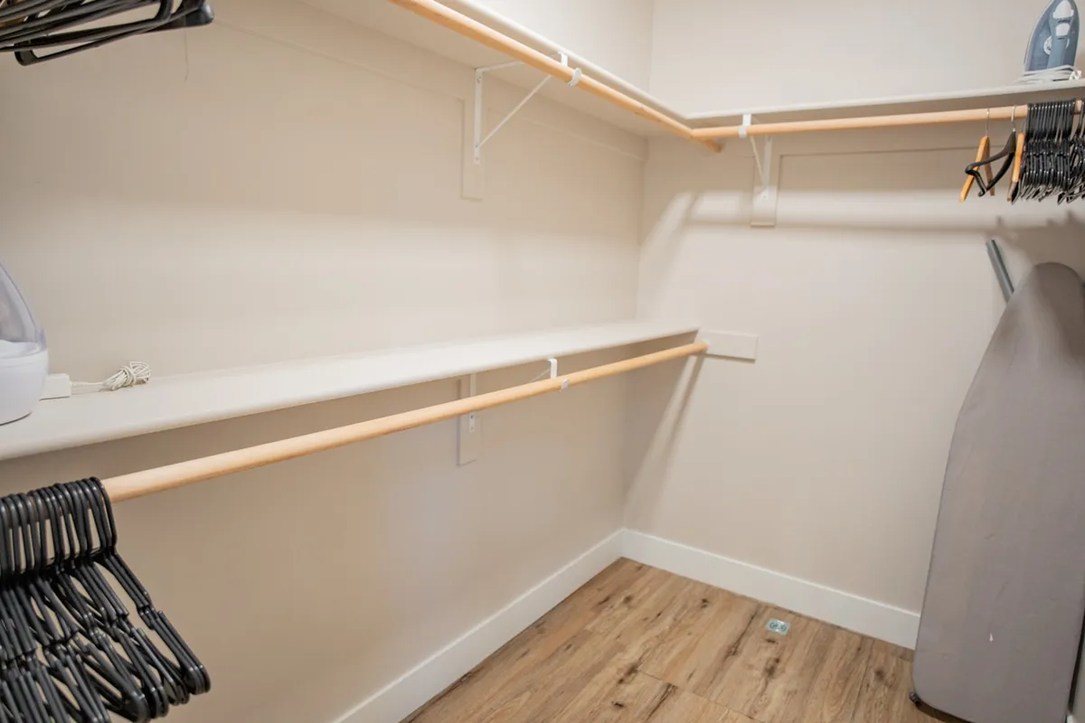 A well-organized mudroom or storage area with clothes hangers, shelves, an ironing board, and a steam iron. The mood is practical, highlighting thoughtful organization for outdoor or seasonal gear.