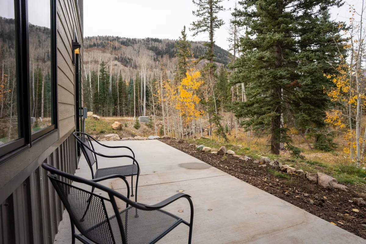 Two black chairs are set up facing a stunning mountain view, surrounded by colorful autumn trees. The scene invites peaceful moments outdoors, such as sipping coffee at sunrise or simply taking in the changing seasons and natural beauty.
